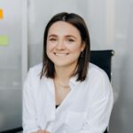 Confident woman in office sitting at desk with laptop and sticky notes.